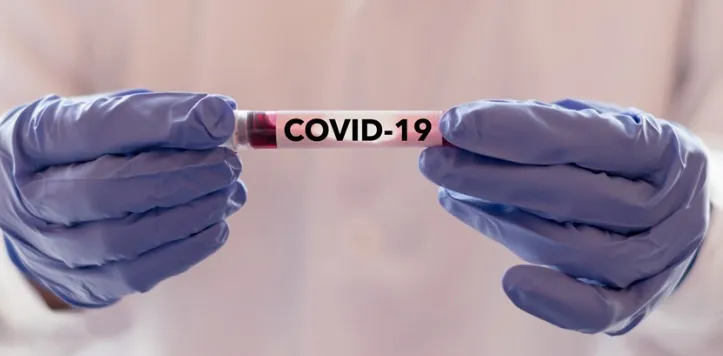 Handen in handschoenen met een buisje met het opschrift COVID-19
